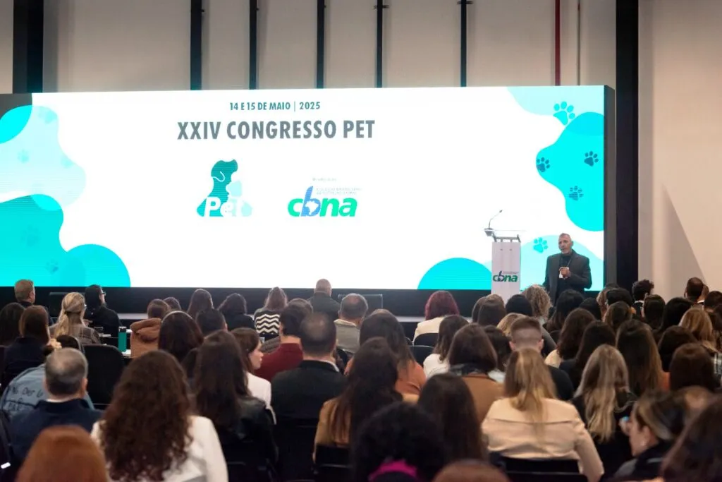 Palestrante em congresso do CBNA diante de plateia, com telão do Congresso PET ao fundo
